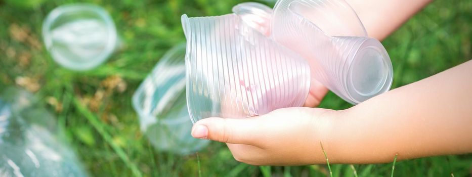 Child's hands clean the park from used plastic utensils in the grass