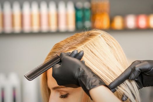 Hairdresser's hand combs female hair before dyeing in a beauty salon