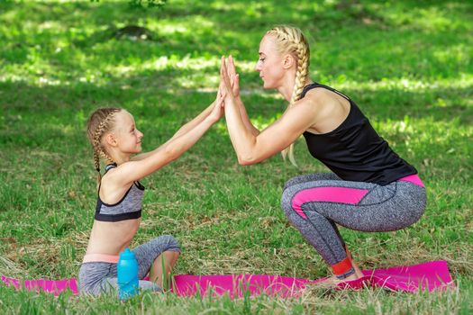 Mother and daughter doing sports exercises on the mat in the park outdoor