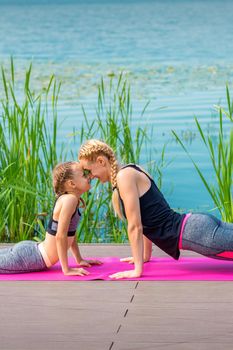 Mother and daughter doing sports exercises on the pier near the water outdoor