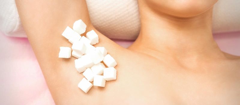 Sugaring concept. White sugar cubes lying on the armpit of a young female