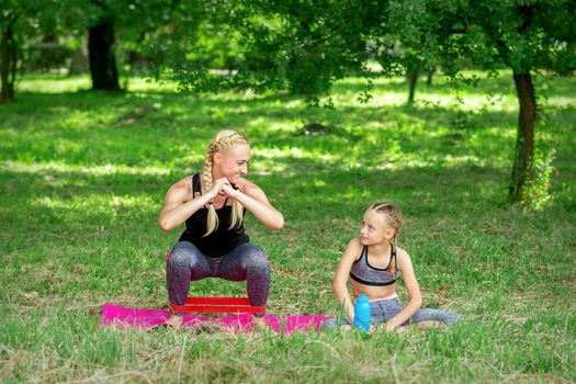 Mother and daughter doing sports exercises on the mat in the park outdoor