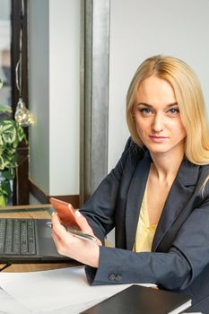 Portrait of a young caucasian businesswoman with a smartphone and laptop at the table looking at the camera