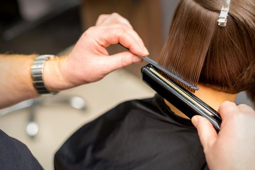 Close up of the hairdresser straightening the short hair of a female client with a hair straightening iron in a beauty salon