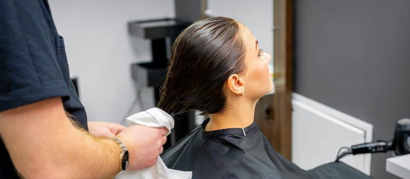 The hairdresser dries the washed hair with a towel to a beautiful young brunette woman at a beauty salon