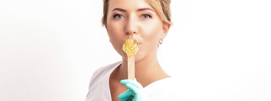 Portrait of female cosmetologist holds a wooden stick with a wax covering her lips on white background