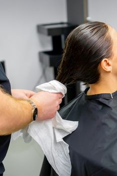 The hairdresser dries the washed hair with a towel to a beautiful young brunette woman at a beauty salon