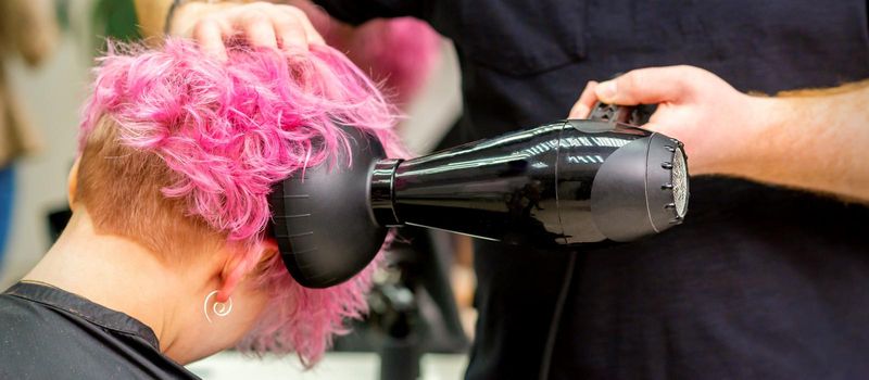 Close up of hairdresser drying short pink or red hair with a hairdryer in a beauty salon