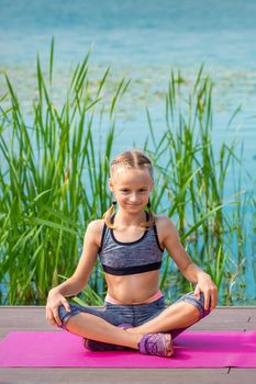 Child in sportswear sitting on the mat on the pier near the water outdoor
