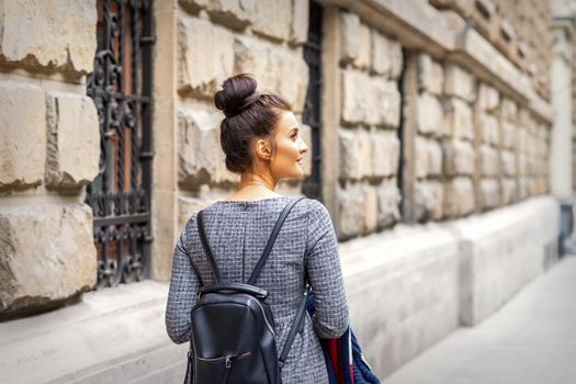 Back view of a young woman with a backpack walks in a European city