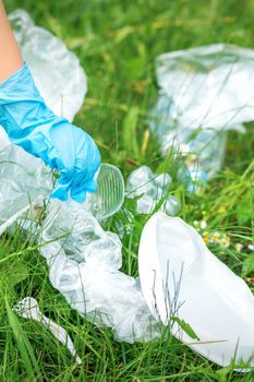 Child's hand cleans park from plastic utensils in the grass in the park
