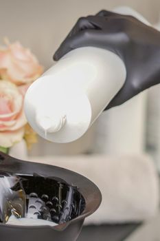 Hairdresser's hand mix hair dye in a black bowl in a beauty salon. Selective focus