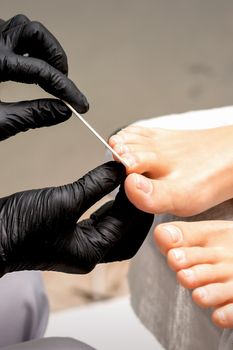 Pedicure master's hands in protective rubber gloves file female toenails with a nail file in a beauty salon
