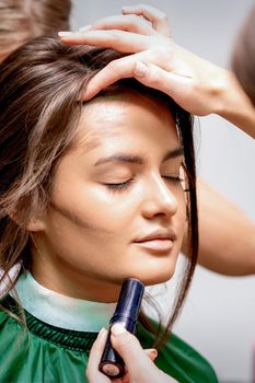 The hairdresser and makeup artist are doing hairstyle and make-up for a beautiful young caucasian woman in a beauty salon