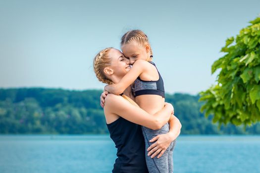 Mother embracing her daughter near the pond wearing sportswear outdoors