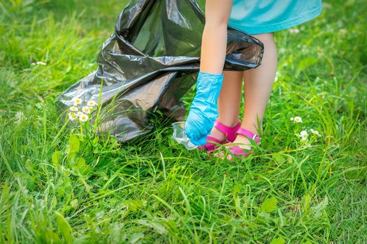Child's hand cleans park from plastic utensils in the grass in the park