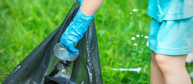 Child's hand puts plastic debris in the garbage bag in the park