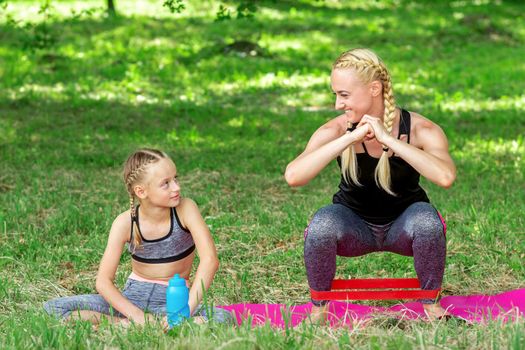 Mother and daughter doing sports exercises on the mat in the park outdoor