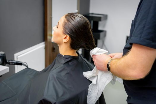 The hairdresser dries the washed hair with a towel to a beautiful young brunette woman at a beauty salon
