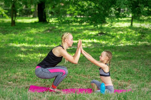 Mother and daughter doing sports exercises on the mat in the park outdoor