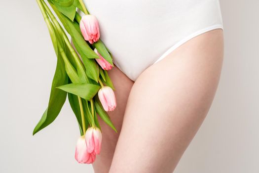 Bikini area of a young woman wearing a white underwear with pink tulips on white background