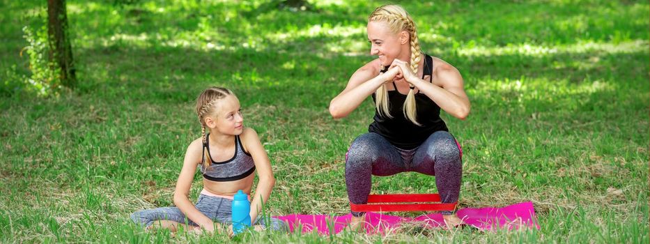 Mother and daughter doing sports exercises on the mat in the park outdoor