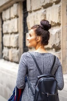 Back view of a young woman with a backpack walks in a European city
