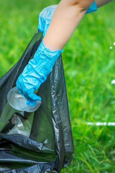 Child's hand puts plastic debris in the garbage bag in the park