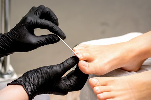 Pedicure master's hands in protective rubber gloves file female toenails with a nail file in a beauty salon