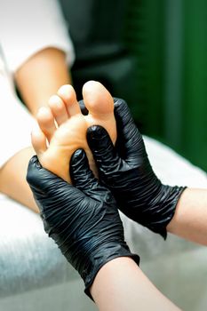 Beautician in protective rubber gloves doing massage on the sole of the female foot in a spa beauty salon