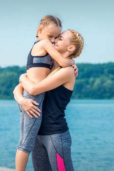 Mother embracing her daughter near the pond wearing sportswear outdoors