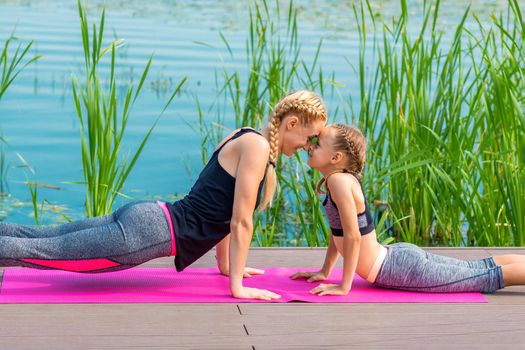 Mother and daughter doing sports exercises on the pier near the water outdoor