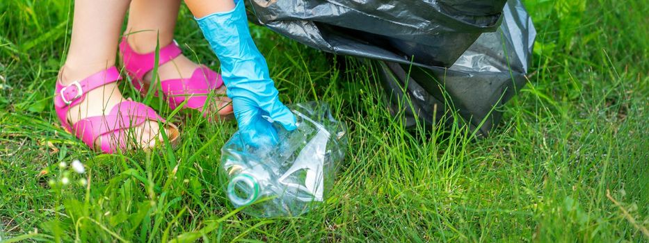 Child's hand cleans park from plastic utensils in the grass in the park. Selective focus