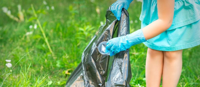 Child's hand puts plastic debris in the garbage bag in the park