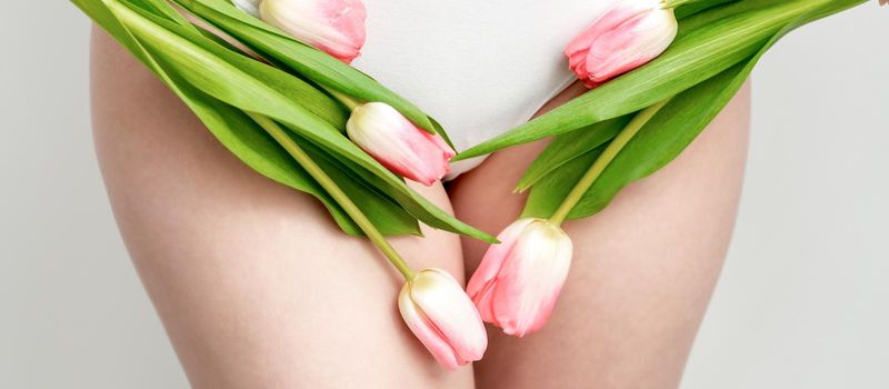 Bikini area of a young woman wearing a white underwear with pink tulips on white background