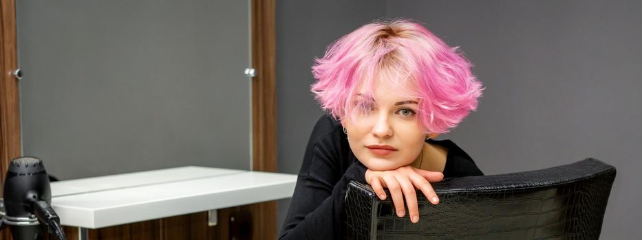 Portrait of a beautiful young caucasian woman with new short pink hairstyle sitting in a chair at a beauty salon