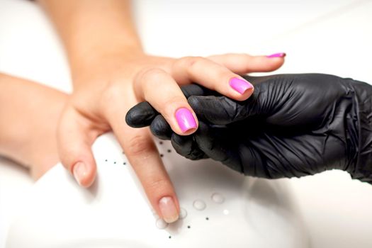 Manicure master's hand holds a female finger with purple nail polish while painting the nails in a nail salon