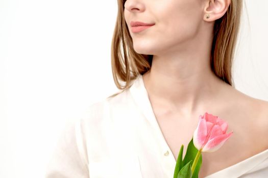 Half face portrait of a beautiful young caucasian woman with one pink tulip on white background