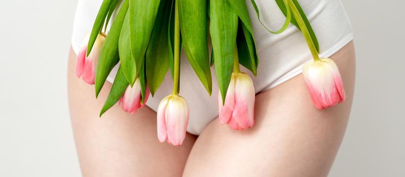 Bikini area of a young woman wearing a white underwear with pink tulips on white background