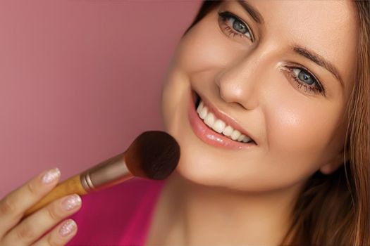 Beautiful young woman applying cosmetic powder product with make-up bamboo brush, beauty, makeup and skincare cosmetics model face portrait on pink background, closeup