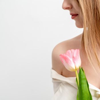 Half face portrait of a beautiful young caucasian woman with one pink tulip on white background