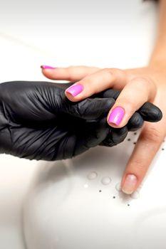 Manicure master's hand holds a female finger with purple nail polish while painting the nails in a nail salon
