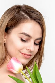 A portrait of a happy young caucasian woman with closed eyes and one pink tulip against a white background with copy space