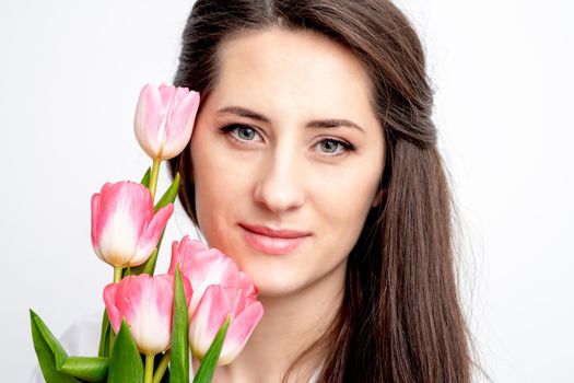 Portrait of a happy young caucasian woman with pink tulips against a white background