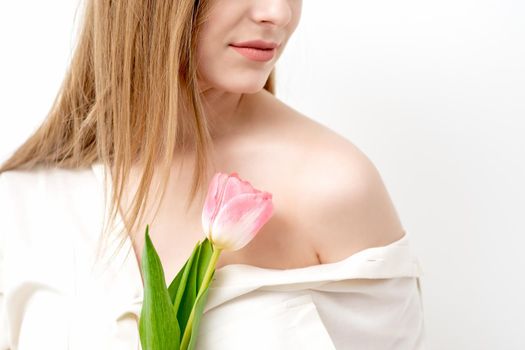 Half face portrait of a beautiful young caucasian woman with one pink tulip on white background