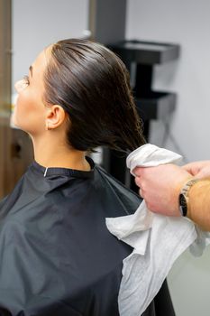 The hairdresser dries the washed hair with a towel to a beautiful young brunette woman at a beauty salon