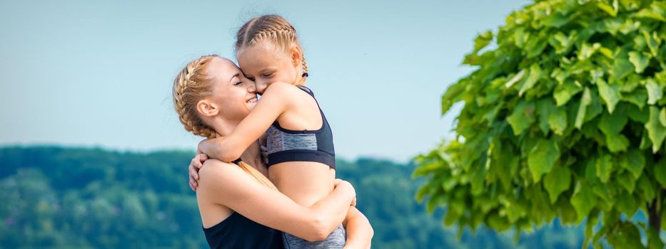 Mother embracing her daughter wearing sportswear outdoors. Woman and child embracing outdoor