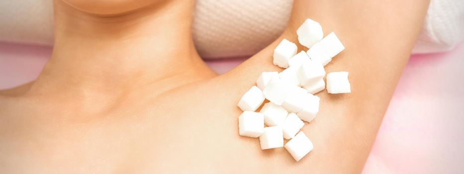 Sugaring concept. White sugar cubes lying on the armpit of a young female