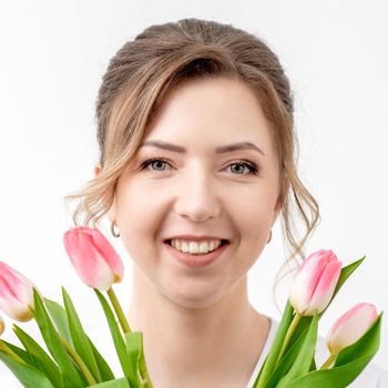 Portrait of a happy young caucasian woman with pink tulips against a white background