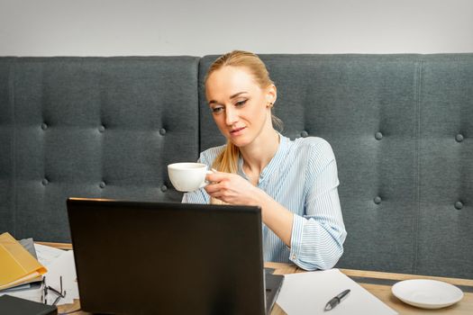 Portrait of a young businesswoman using laptop sitting at the table with a cup of coffee in a cafe